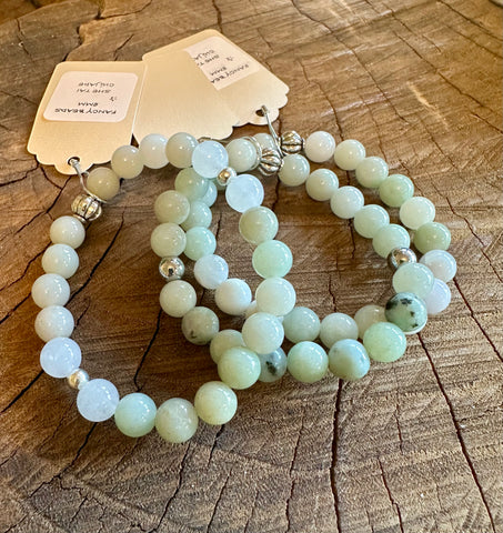 My Two Daughters Jewelry - A bracelet made with green beads and silver accents, displayed on a wooden surface with a tag attached.
