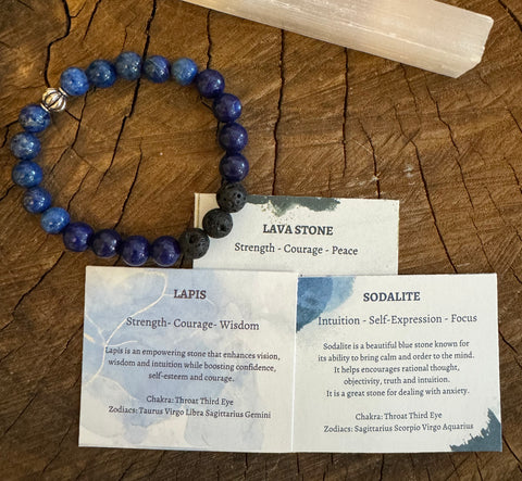 My Two Daughters Jewelry - A bracelet made of blue lapis and black lava stone beads, displayed on a wooden surface with information cards detailing the properties of each stone.