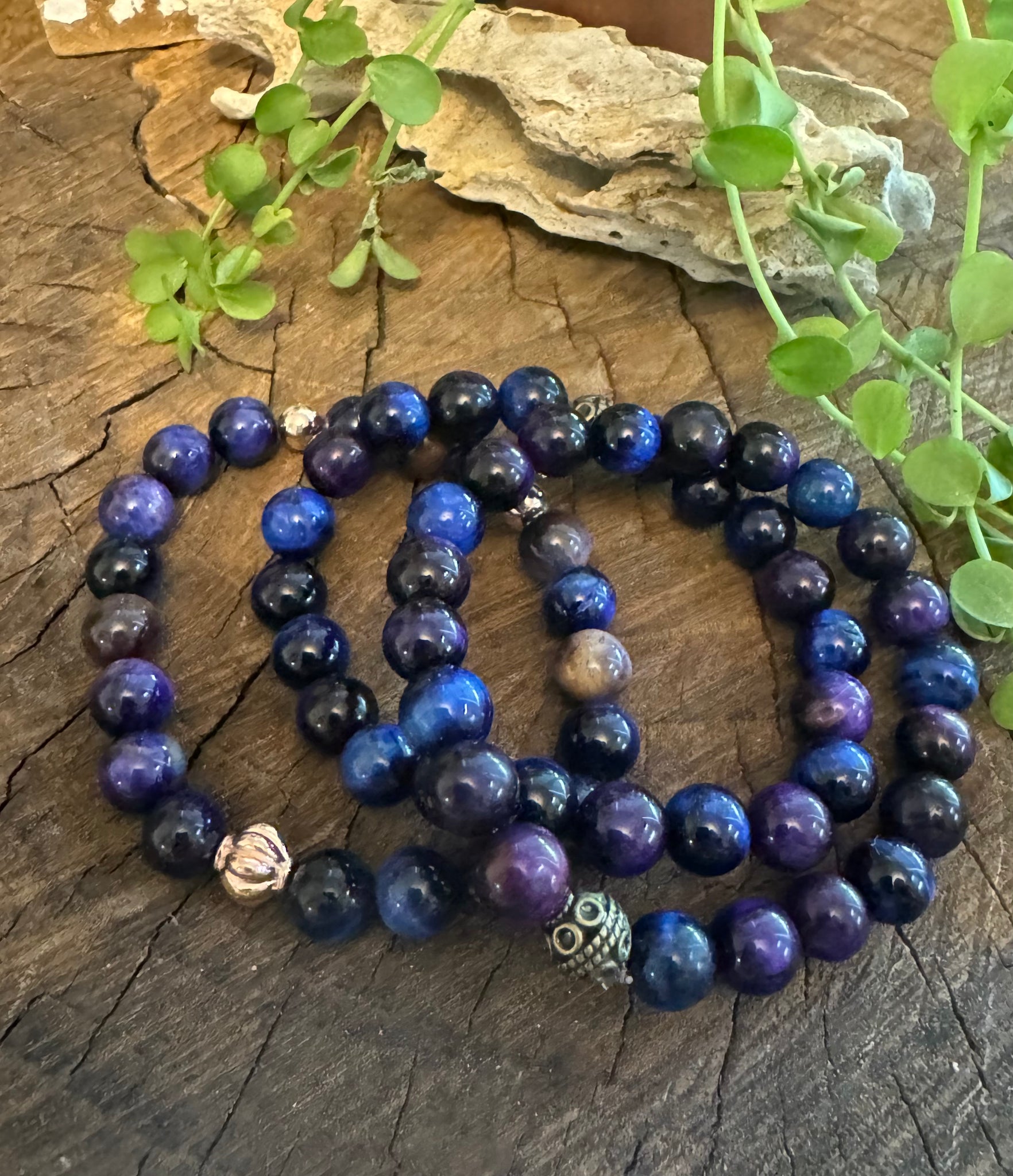 My Two Daughters Jewelry - A necklace with round blue beads and multicolored accents, displayed on a wooden surface with foliage in the background.