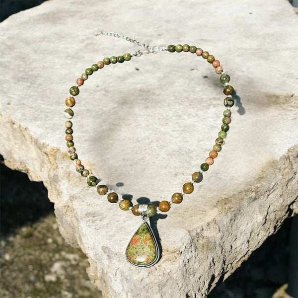 My Two Daughters Jewelry - A beaded necklace with green and orange marbled beads and a matching teardrop pendant, displayed on a textured stone slab outdoors.