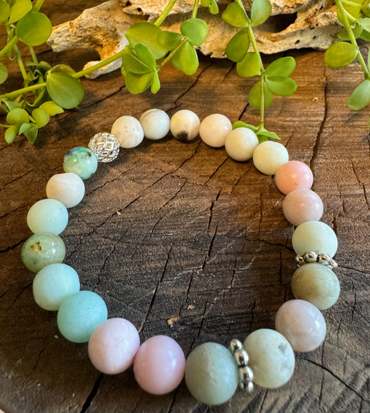 My Two Daughters Jewelry - A bracelet with round beads in shades of green, blue, and pink, with metallic silver accents, displayed on a wooden surface with foliage in the background.