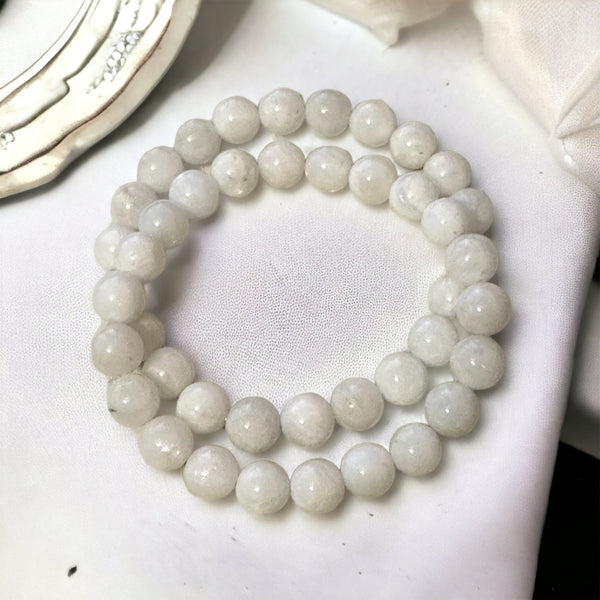 My Two Daughters Jewelry - A bracelet made of round white moonstone beads laid out on a white surface.