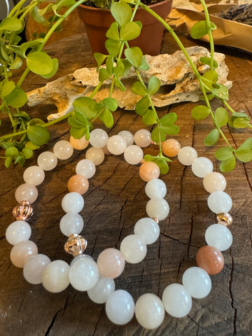 My Two Daughters Jewelry - A bracelet made of pink and white beads, with variations in color and design, displayed on a wooden surface with green leaves in the background.