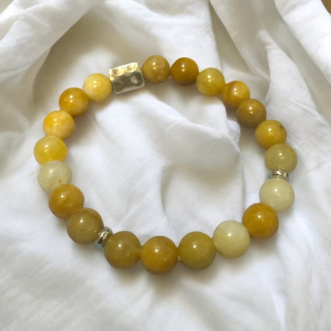 My Two Daughters Jewelry - A bracelet made of round yellow beads with a silver clasp, displayed on a white fabric surface.