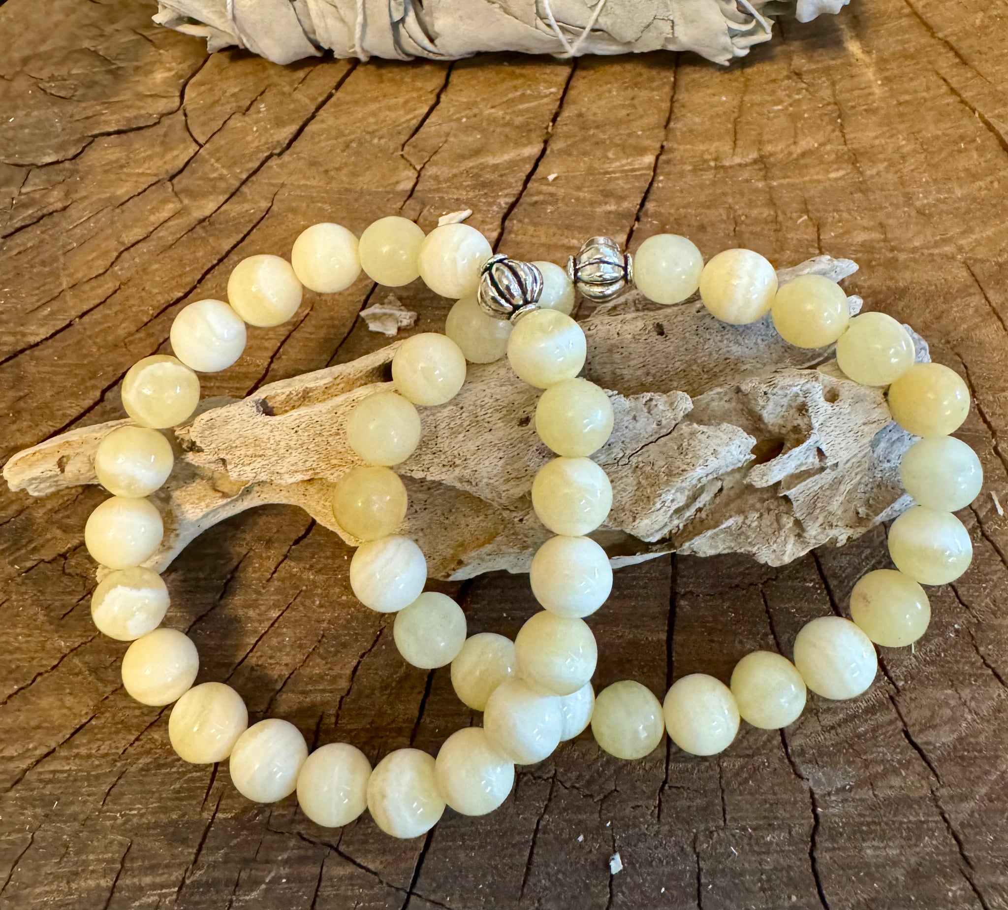 My Two Daughters Jewelry - A yellow calcite bracelet laid out on a wooden surface, with the bracelet displaying smooth, round beads and a silver clasp.
