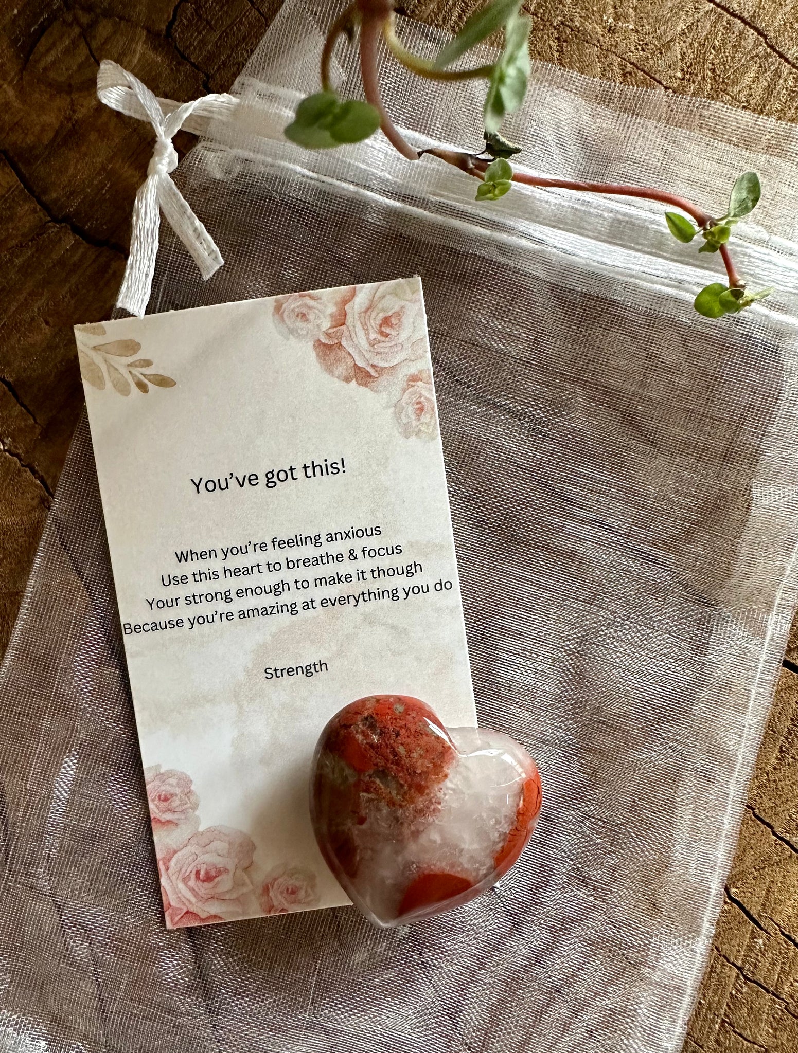 Kelowna Crystal Cave - A 30mm red agate heart-shaped stone with a card and a clear organza bag on a wooden surface.