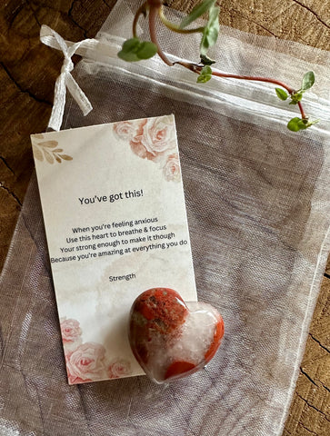 Kelowna Crystal Cave - A 30mm red agate heart-shaped stone with a card and a clear organza bag on a wooden surface.