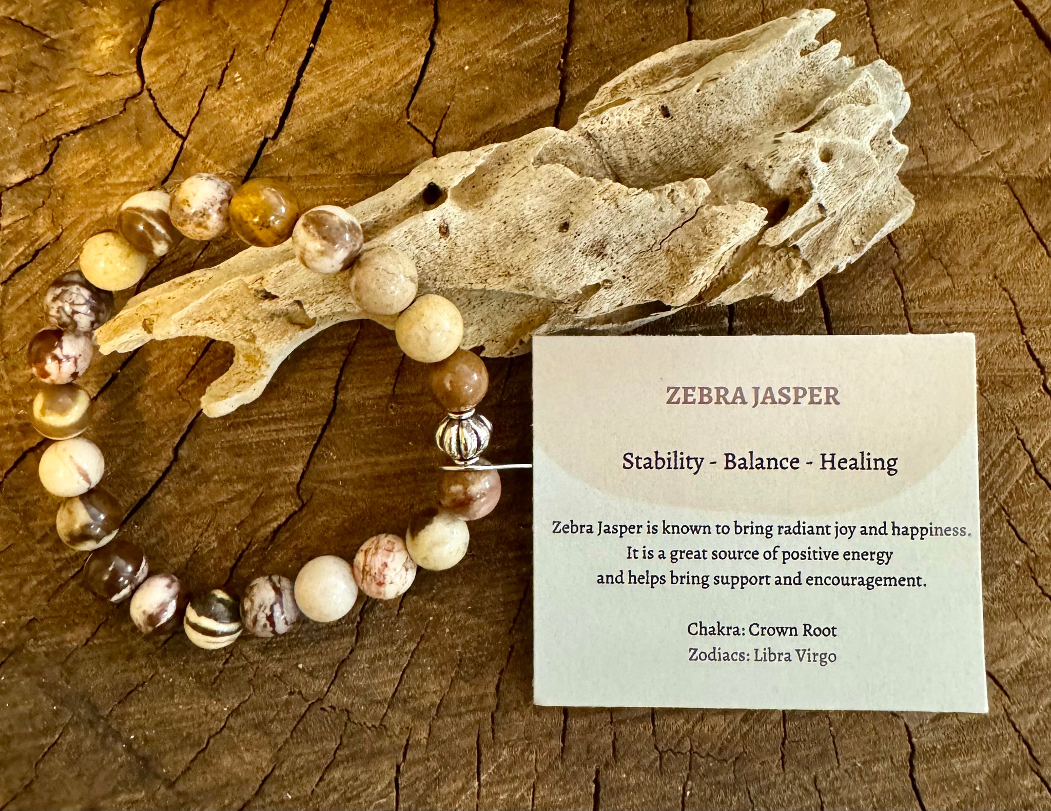 My Two Daughters Jewelry - A Zebra Jasper Bracelet displayed alongside a piece of driftwood and a card describing the stone's properties, including stability, balance, and healing.