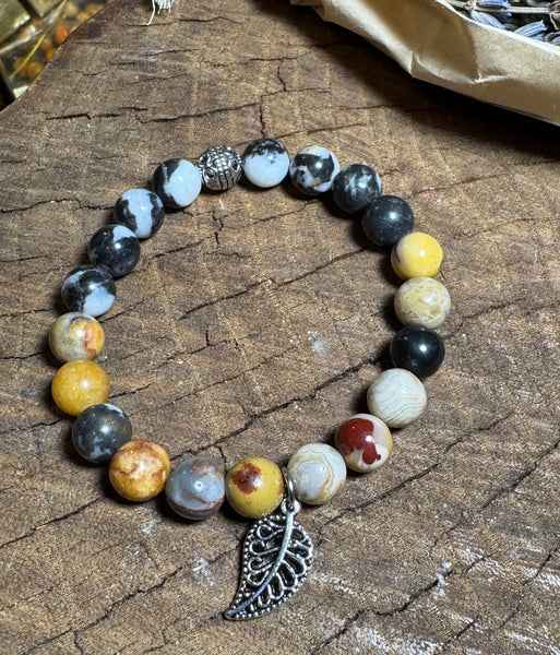 My Two Daughters Jewelry - A bracelet made with black and white zebra jasper stones, featuring a silver-colored clasp and a silver feather charm, displayed on a wooden surface.