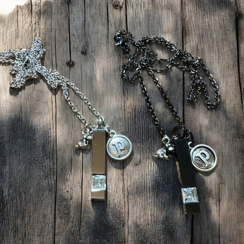 Blazin Creationz - Two pet memory necklaces laid out on a wooden surface, one in silver and one in black, each with a tag that reads 'P' and a star-shaped charm.