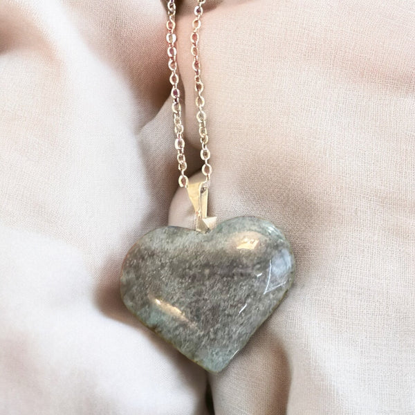 My Two Daughters Jewelry - A heart-shaped polished stone pendant necklace on a delicate chain, resting on soft beige fabric.