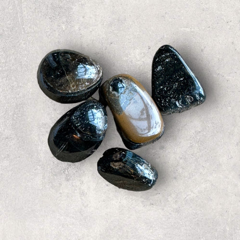 Kelowna Crystal Cave - A collection of polished black sardonyx stones of various shades placed on a grey surface.