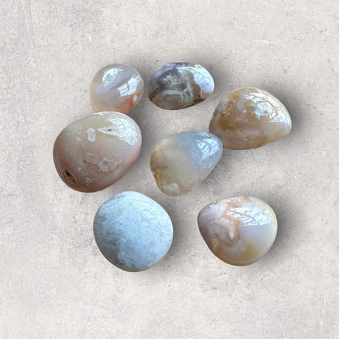 Kelowna Crystal Cave - A collection of Flower Agate tumbles on a textured background, displaying patterns and colors typical of the stone.