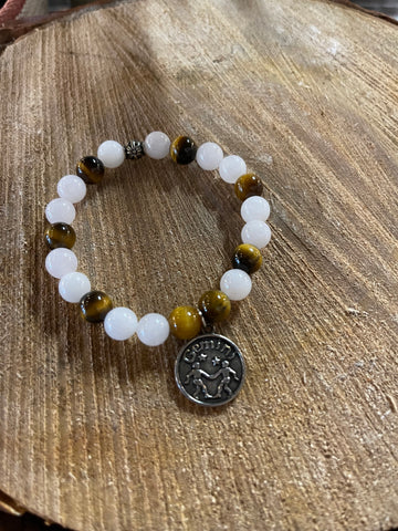 My Two Daughters Jewelry - A bracelet with white and yellow beads, and a silver-colored Gemini zodiac charm, displayed on a wooden surface.