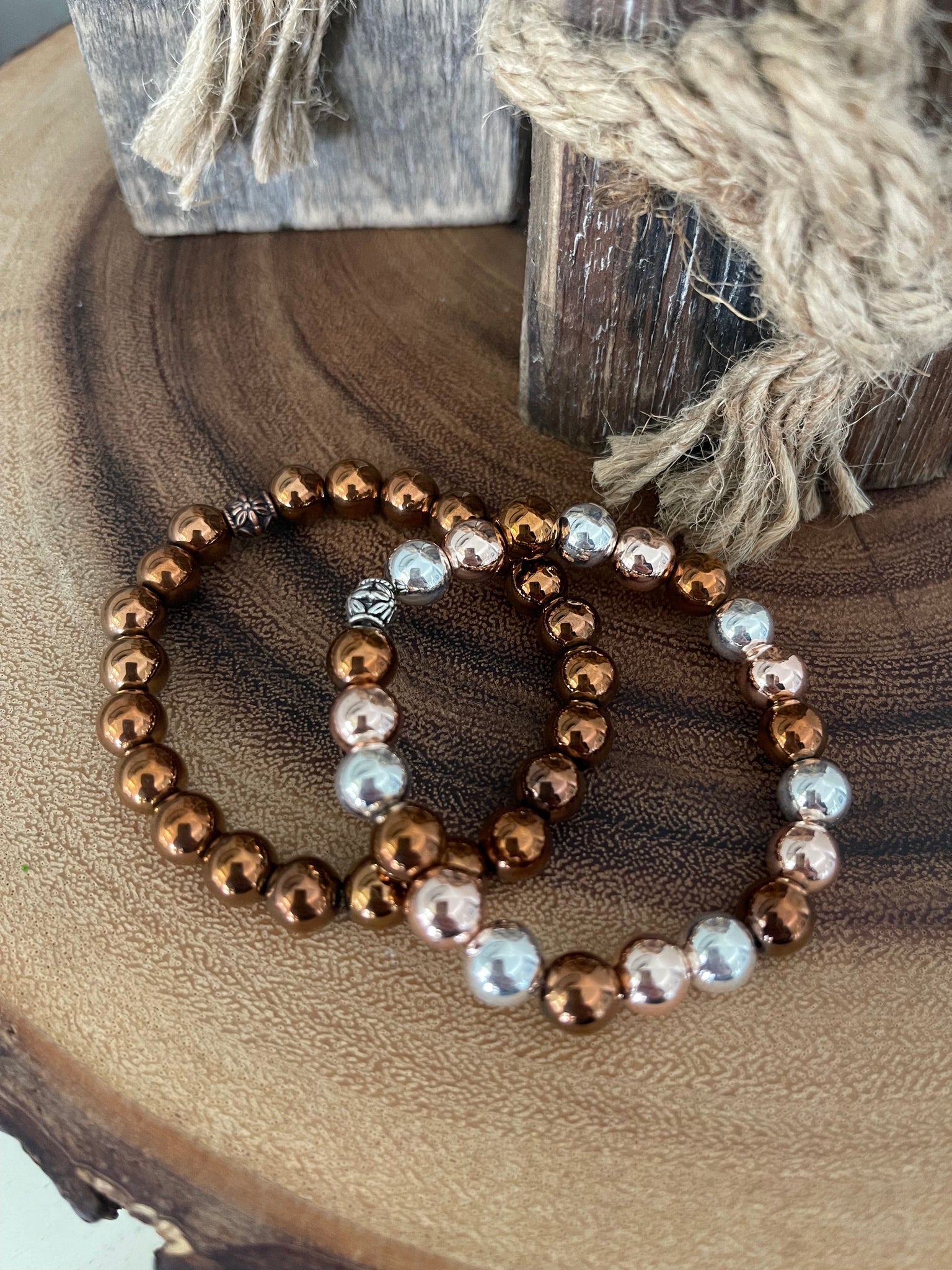 My Two Daughters Jewelry - A bracelet made with red copper and hematite beads displayed on a wooden surface.