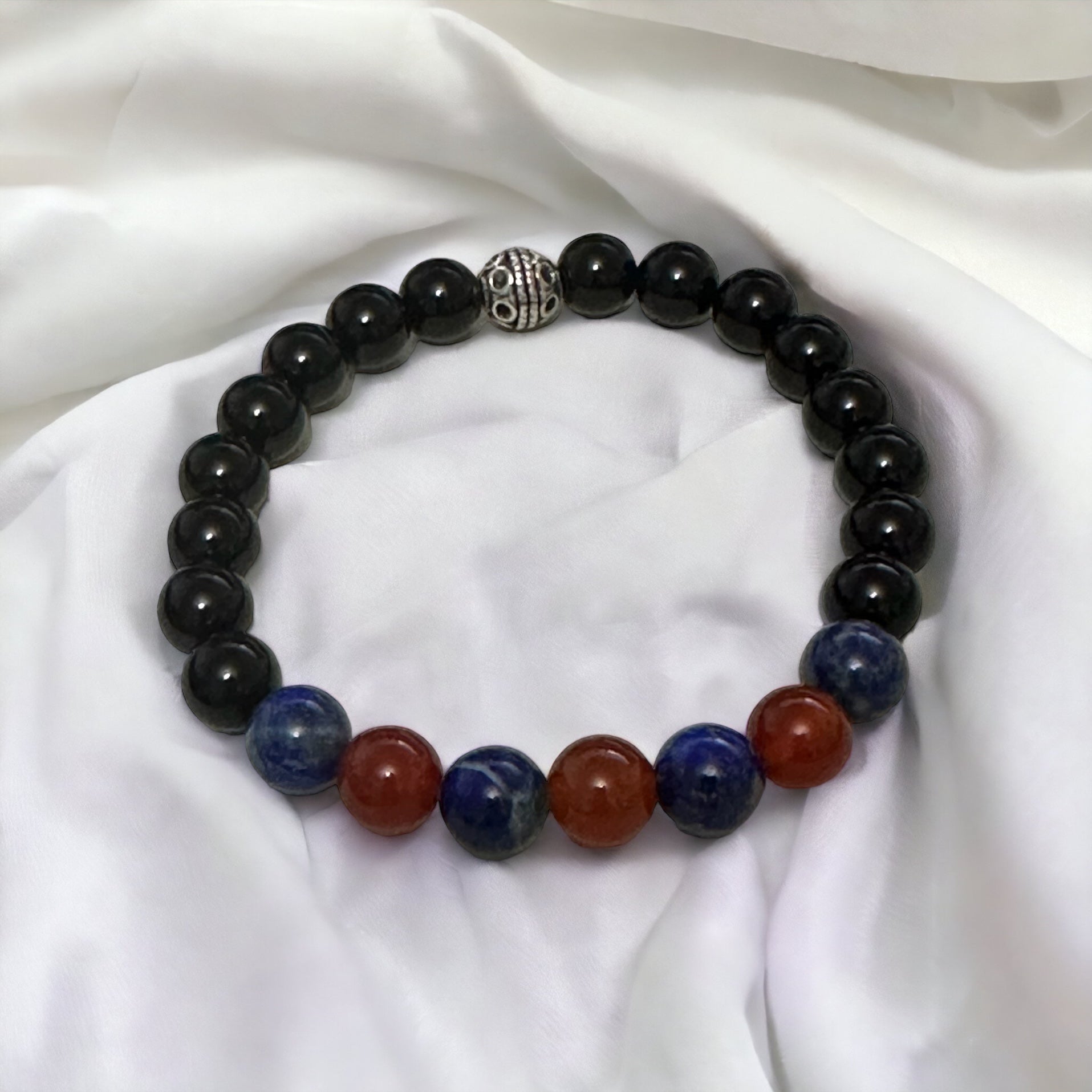 My Two Daughters Jewelry - A bracelet with black onyx beads, interspersed with red agate and lapis lazuli beads, displayed on a white fabric surface.