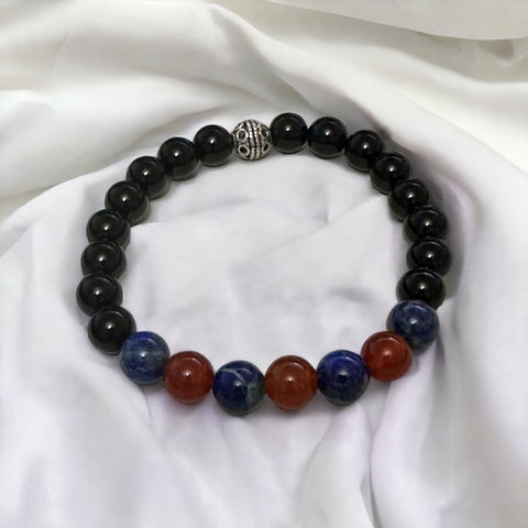 My Two Daughters Jewelry - A bracelet with black onyx beads, interspersed with red agate and lapis lazuli beads, displayed on a white fabric surface.