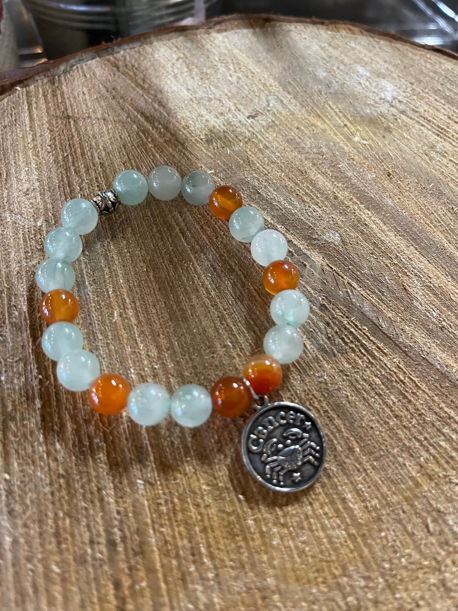 My Two Daughters Jewelry - A bracelet with round beads in shades of orange and green, featuring a silver-colored Cancer zodiac charm.