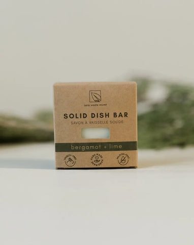Zero Waste Mvmt - A solid dish bar packaged in a brown cardboard box with a label that reads 'SOLID DISH BAR' and 'bergamot + lime'. The box is placed on a white surface with a blurred background.