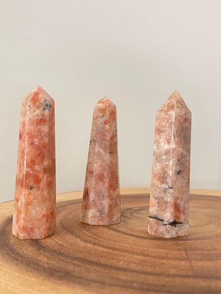 Kelowna Crystal Cave - Three polished sunstone crystal points of varying sizes placed on a wooden surface.